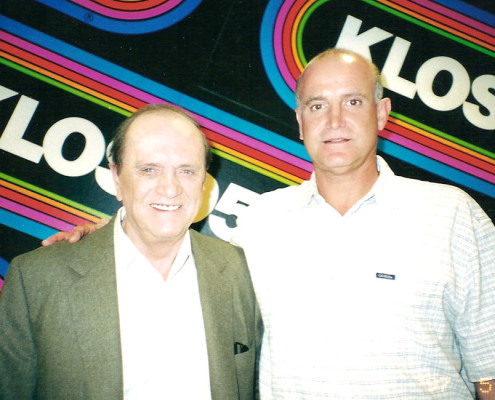 Two men standing next to each other in front of a colorful sign.