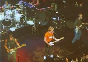 A group of people on stage with guitars and drums.