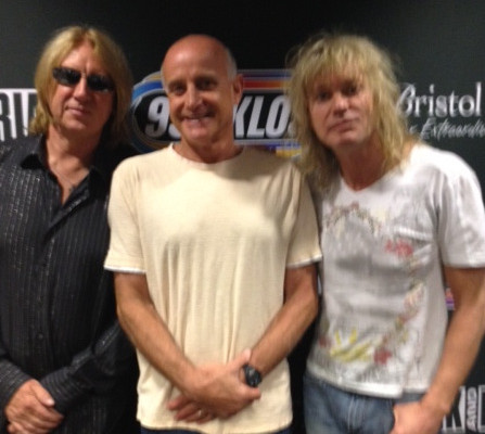 Three men posing for a photo in front of a radio station.