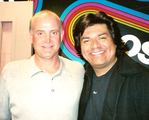 Two men posing for a photo in front of a radio station.