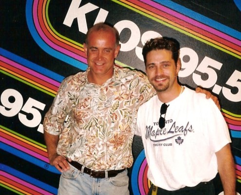 Two men posing for a picture in front of a colorful sign.