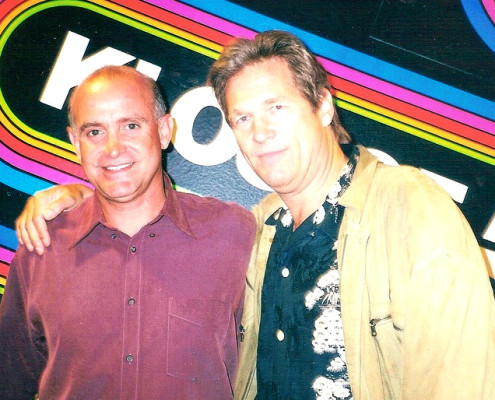 Two men standing next to each other in front of a colorful sign.