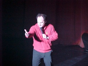 A man in a red sweater holding a microphone.