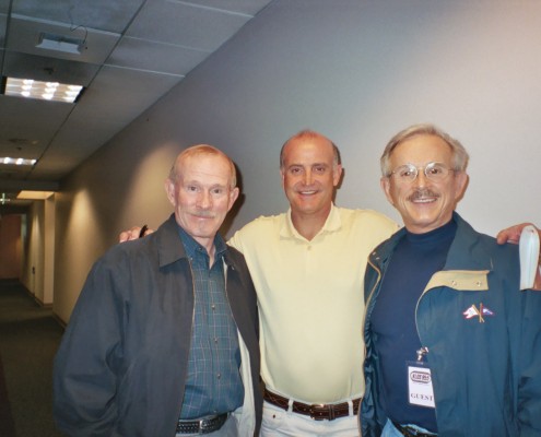 Three men posing for a picture in a hallway.