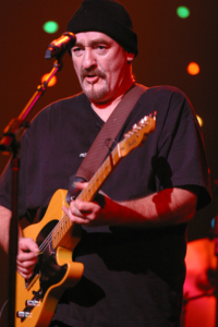 A man with a guitar in front of a microphone.